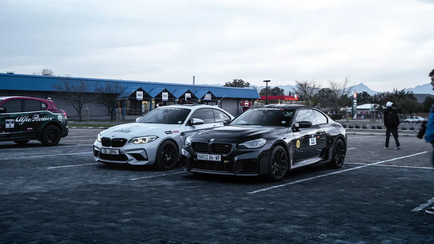 A silver and a black BMW M2 parked side by side at a rally stop