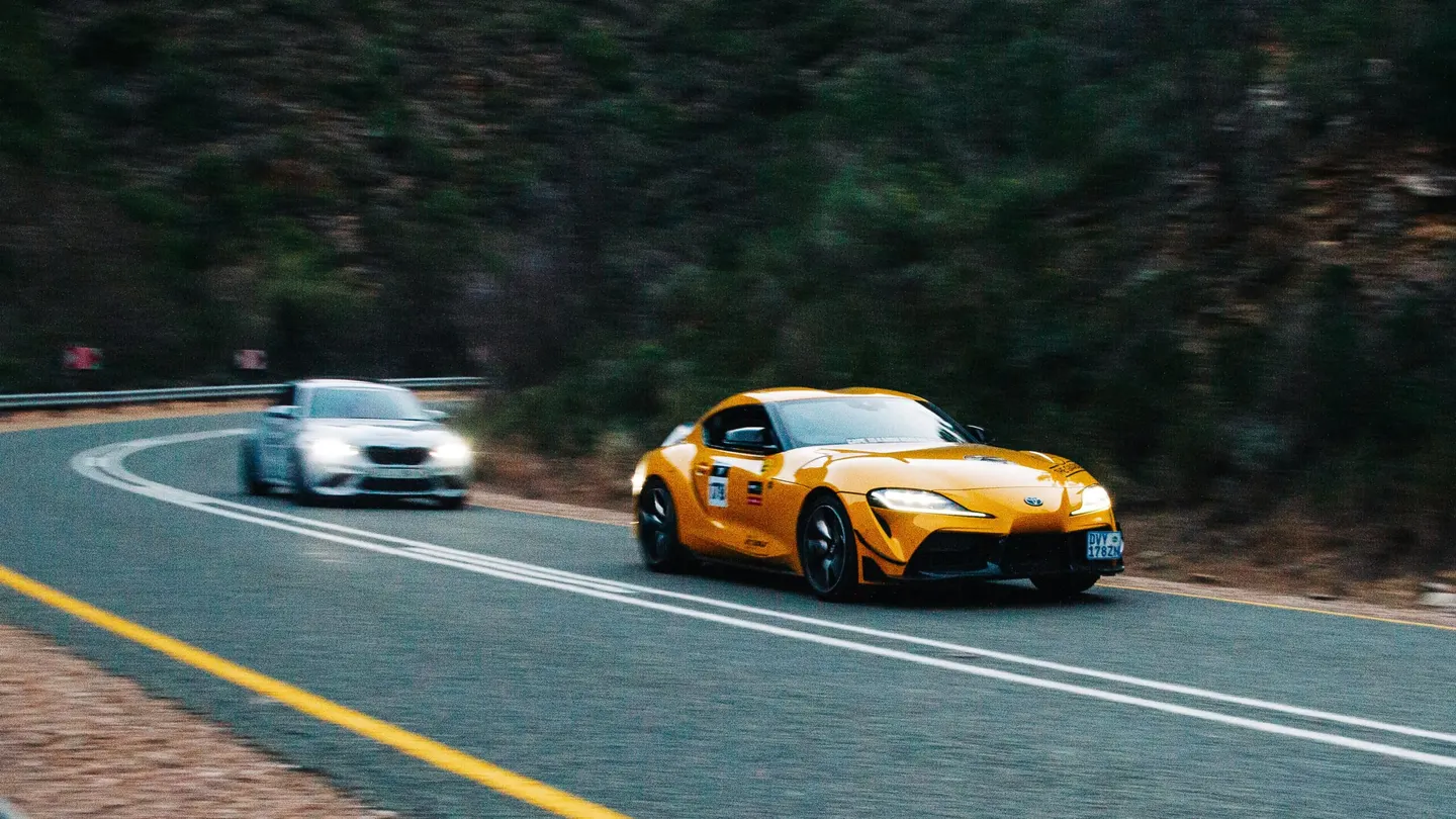 The yellow Supra on a mountain road with a BMW following