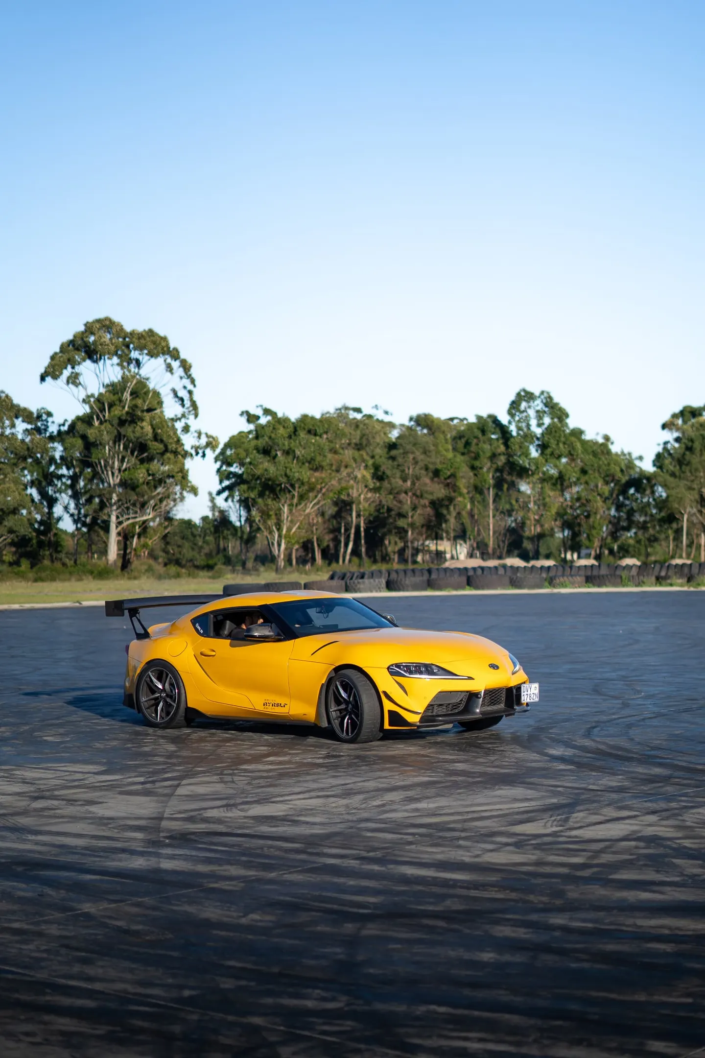 A yellow Toyota Supra on an open tarmac apron at sunrise