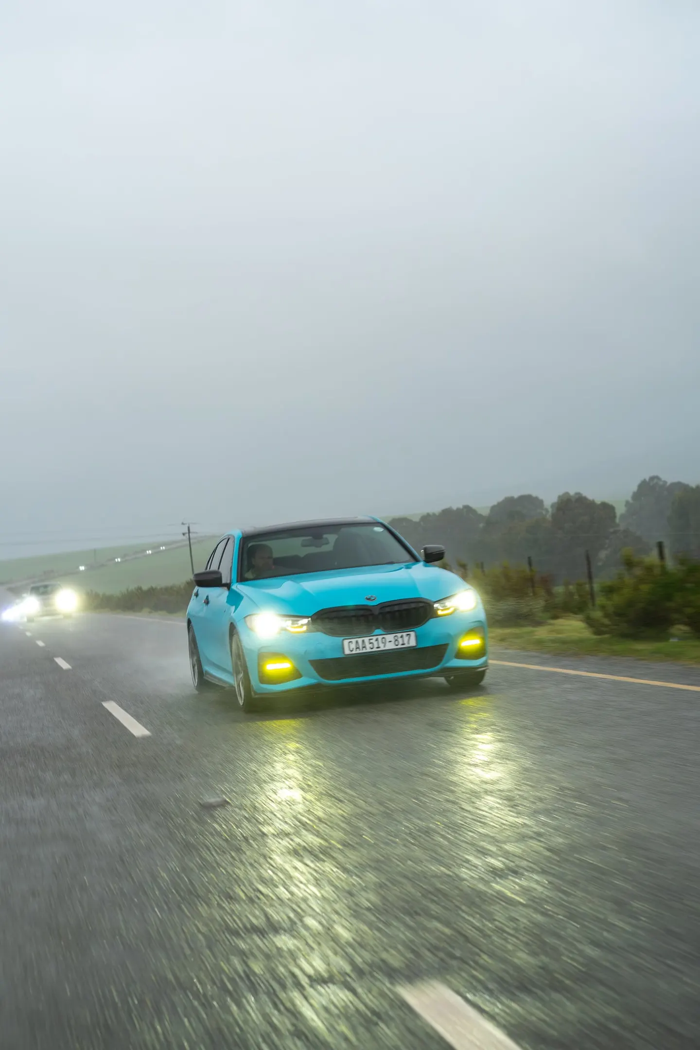 A light blue BMW 3 Series on the wet road