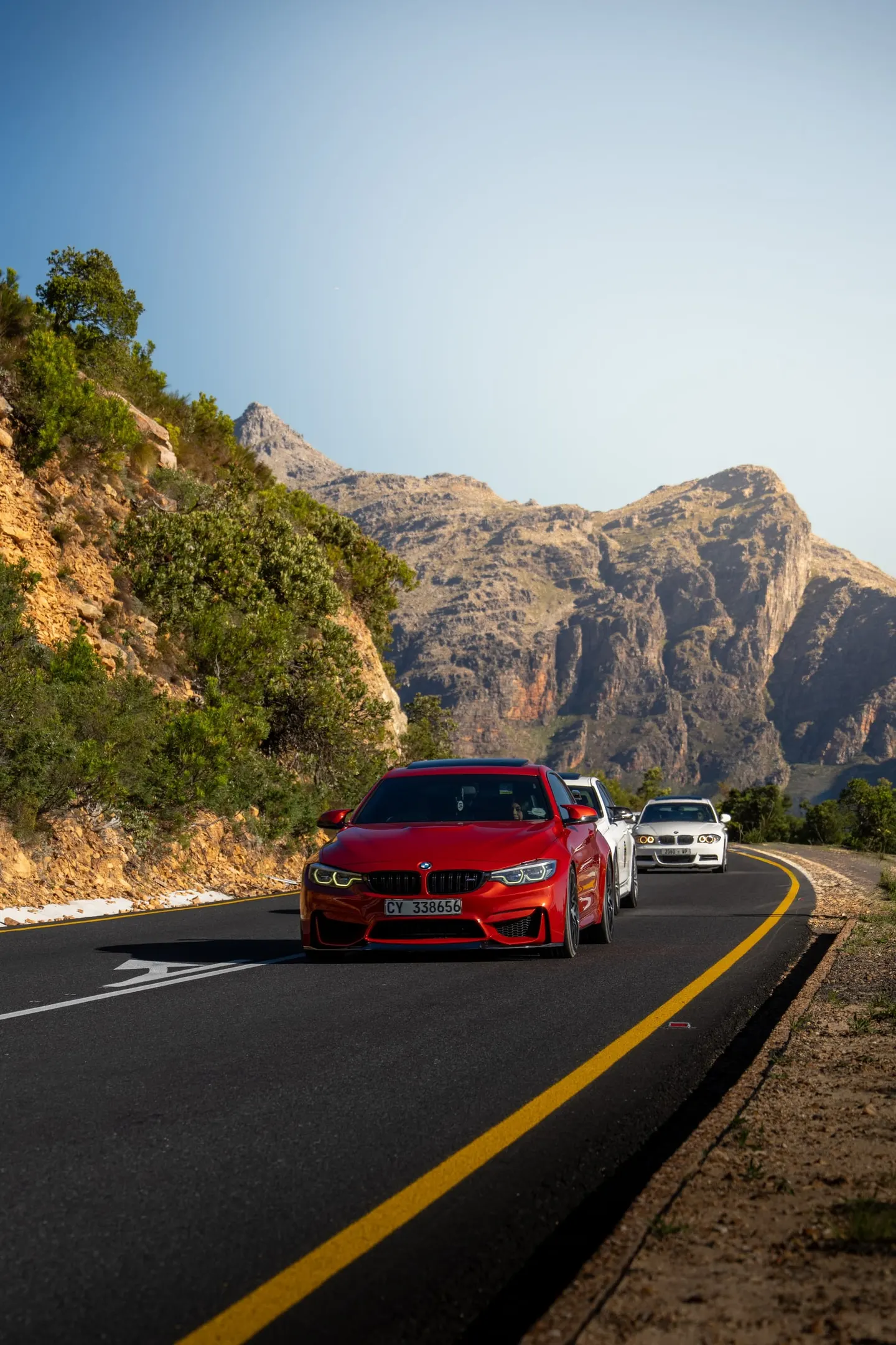 A red BMW leading a line of cars up the mountain pass in late light